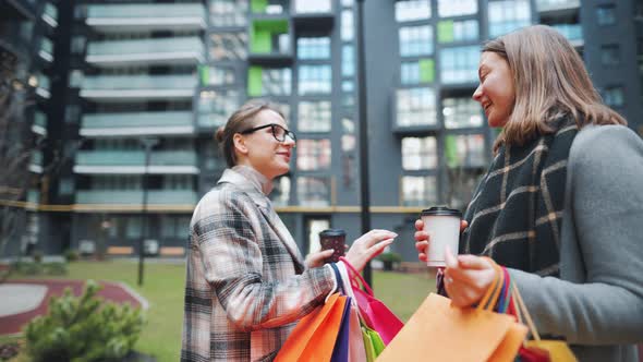 Two Happy Women Stand with Shopping Bags and Takeaway Coffee After a Successful Shopping and Talk