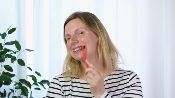 Young Woman with Dental Braces Brushing Teeth on Bathroom Background