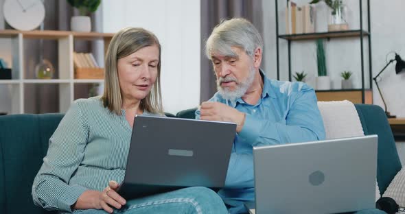 Senior Couple Resting on Comfy Couch with Personal Laptops