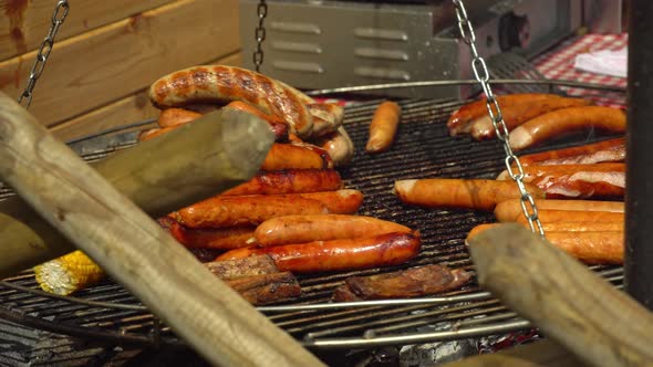 Chef flips sausages Bratwurst roasting with cooking tongs. Street food for picnic and camping. BBQ