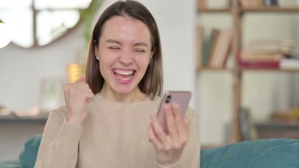 Young Woman Celebrating on Smartphone at Home 