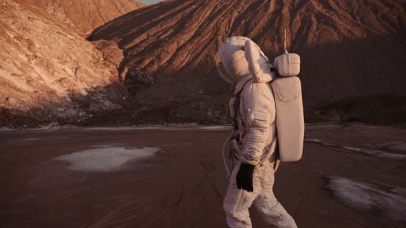 the Astronaut Walks Cautiously Against the Background of the Hills