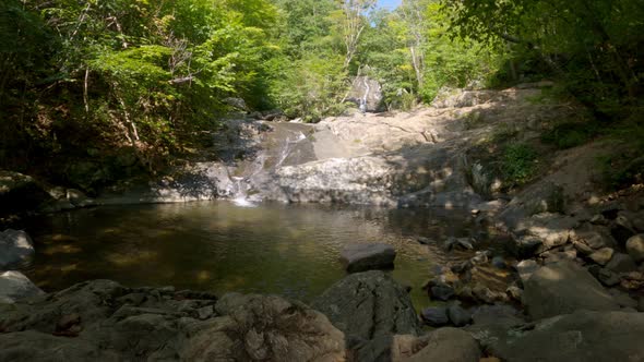 Waterfall flowing into a rock swimming pool on a sunny day, Static