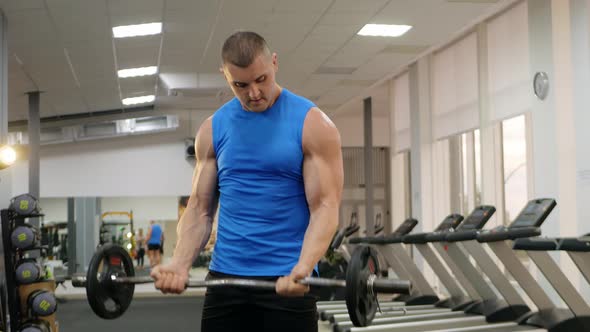 A Young Handsome Coach with a Muscular Body Poses in Gym