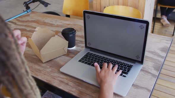 Mixed race man with dreadlocks sitting in cafe with sandwich and laptop with copy space on screen