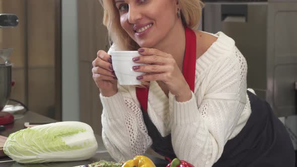 Happy Mature Woman Smiling Having Coffee Resting After Cooking at the Kitchen