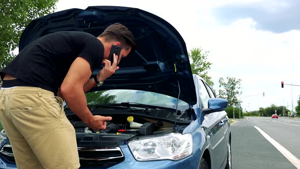 Young Handsome Man Looks on Engine in Car and Phone with Smartphone - Accident