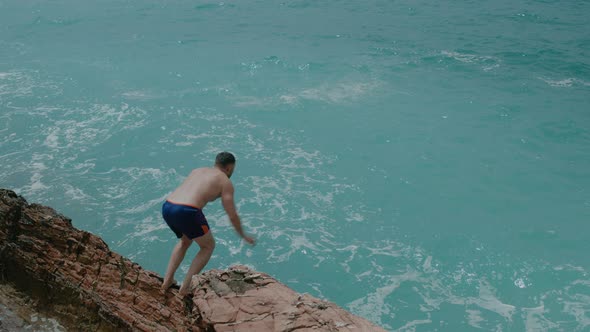 Young man jumping from a stone into the azure Adriatic sea with waves in Montenegro