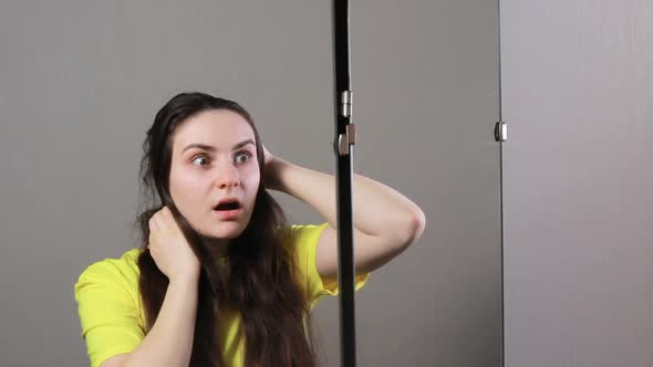 A Woman Under 30 Brunette with Long Hair Stands in Front of a Mirror and Looks at Hair Reflection