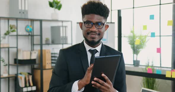 African American Bearded Businessman in Glasses which Posing on Camera while Working on Tablet PC