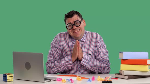 A Man Sits at a Desk in Front of a Laptop and Books Folds His Hands in a Prayer Gesture Asks for