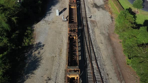 Aerial view of rusty train carsing along a straight set of tracks on a sunny day in the morning.