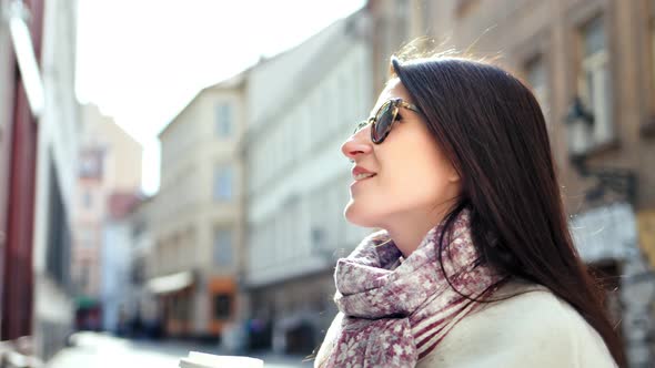 Smiling Stylish Travel Girl in Sunglasses Enjoying Break on Narrow Street Holding Paper Coffee Cup