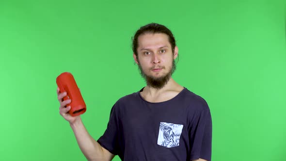 Portrait of a Young Man Listening to Music with a Red Portable Bluetooth Speaker Who Sings Along to