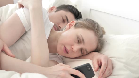 Woman Using Smartphone in Bed While Boyfriend is Sleeping