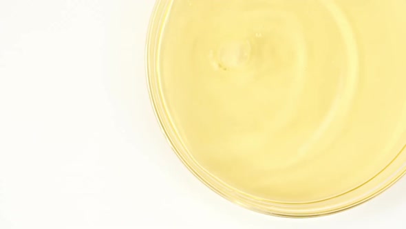 Slow Motion of Transparent Yellow Cosmetic Fluid Dripping Into the Glass Petri Dish alt