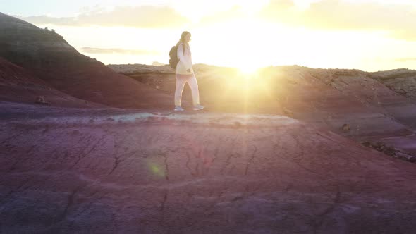 Happy Woman Walking in Colorful Red Desert at Golden Sunset with Sun Rays Flare