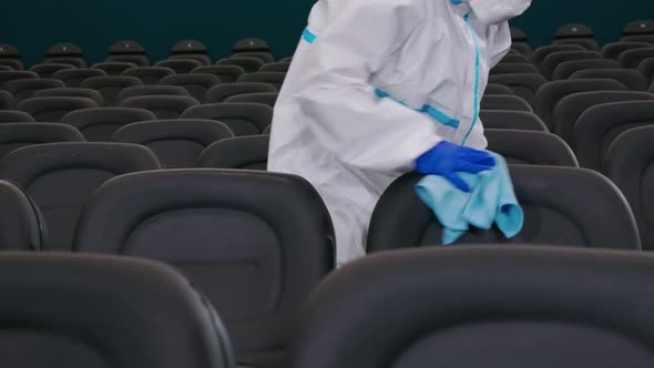 Worker in Protective Uniform Spraying Disinfectant on Chairs