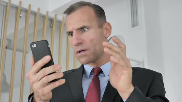 Astonished Middle Aged Businessman Shocked By Result on Smartphone Wondering