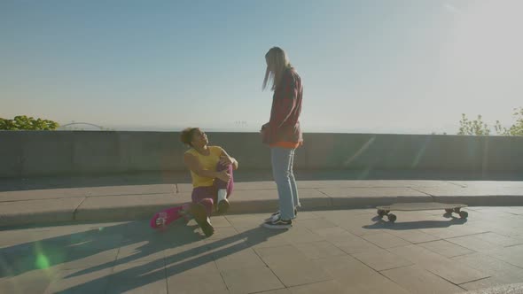 Woman Skateboarder Helping Fallen Skater Friend to Stand Up Outdoors