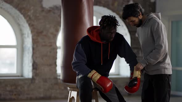 Assistant Helping to Put on Boxing Gloves to a Male Athlete