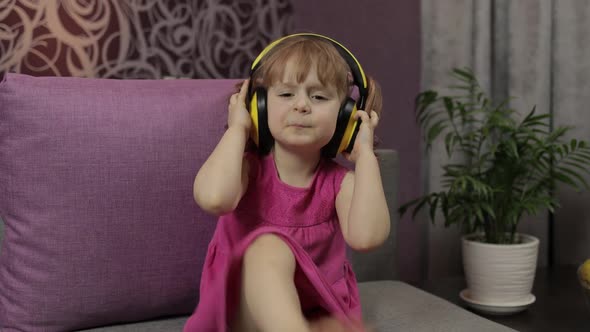 Little Child Girl in Headphones Enjoying Listen Music. Dancing on Sofa at Home