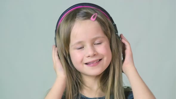 Pretty smiling cild girl listening to music in big pink earphones.