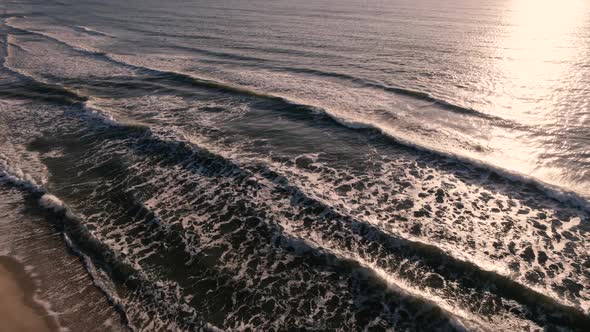 Aerial view of tropical beach, foamy ocean waves washing sand on sunrise.