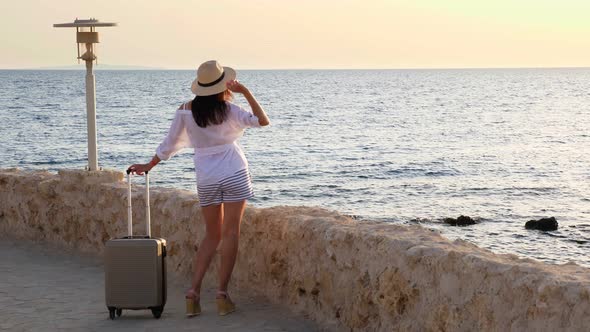 Young Woman in Summer Clothes, Sunglasses and Sun Hat, with Travel Luggage, Stands Along in Empty