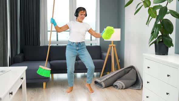 Woman in Headphones Cleaning the House and Having Fun Dancing with a Broom and Washcloth