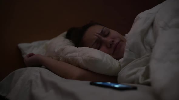 the girl is disturbed by the phone, she switches it to silent mode and continues to sleep