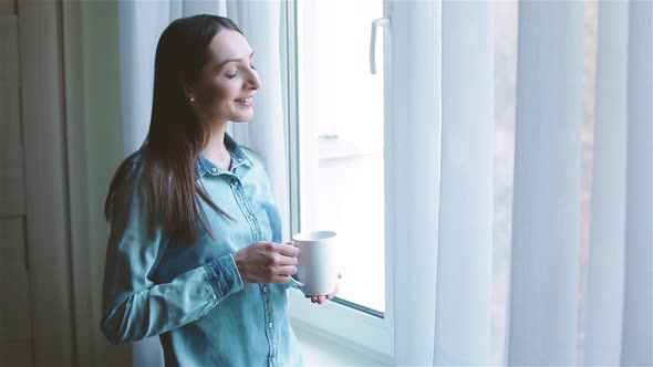 Smiling Lady in Shirt Looks at Cityscape Drinking Coffee