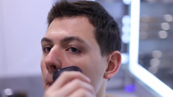 Handsome Man Shaving His Beard in Bathroom By Electrical Modern Razor