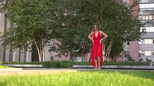 Beautiful Young Girl Dancing on Green Grass Against the Background of a Modern City. She Is Wearing