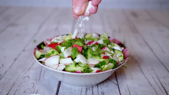 Hands Chef Sprinkles Salt on a Vegetable Salad with Radish Cucumber Greens