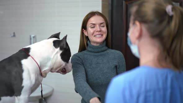 Happy Young Woman Smiling Shaking Hands with Veterinarian As Dog Jumping on Arms Leaving in Slow