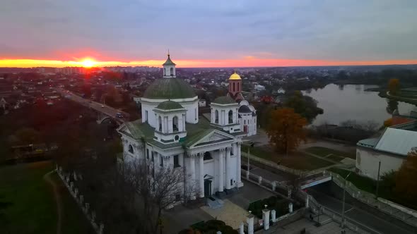 The Camera Circles Around a Small Church on the River Bank in a Small European City at Bright Sunset