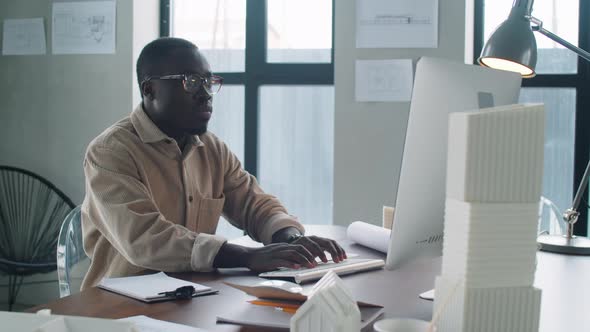 Young Afro-American Architect Working on Computer and Taking Notes