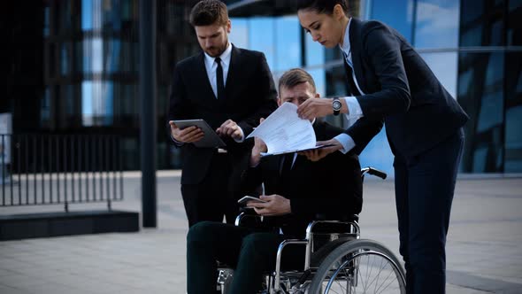 Businessman in a Wheelchair with Colleagues Outside an Office Building Discuss Abut Deal and