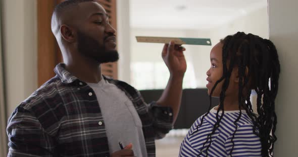 Happy african american father measuring his daughter at home