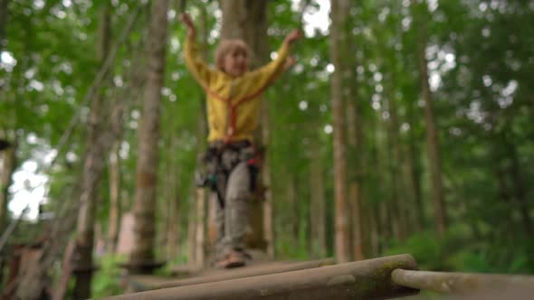 Superslowmotion Shot of a Little Boy in a Safety Harness Climbs on a Route in Treetops in a Forest