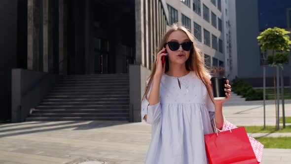 Girl Walking From Mall with Shopping Bags and Talking on Mobile Phone About Sale on Black Friday