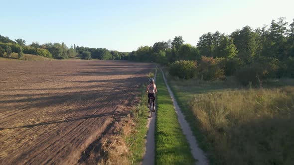 Aerial Shot of Young Sport Woman Rides Bicycle on Countryside Road at Summer Sunset. Happy Holiday