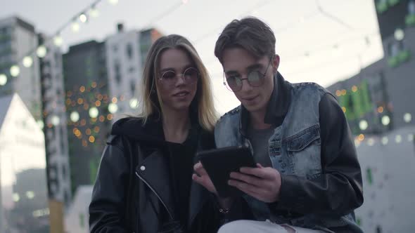 Young People Communicate and Use a Tablet Near a Modern Residential Area Evening in the City Blurry