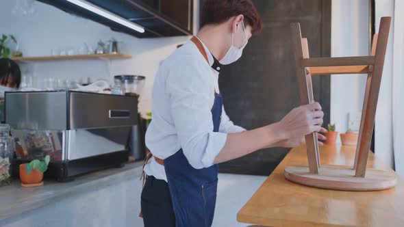 Young waiter put chair on table to clean and arranging furniture after close coffee shop restaurant