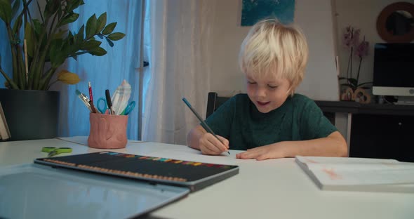 Happy Smiling Child Boy Drawing on Paper Sheet with Color Pencil on Evening