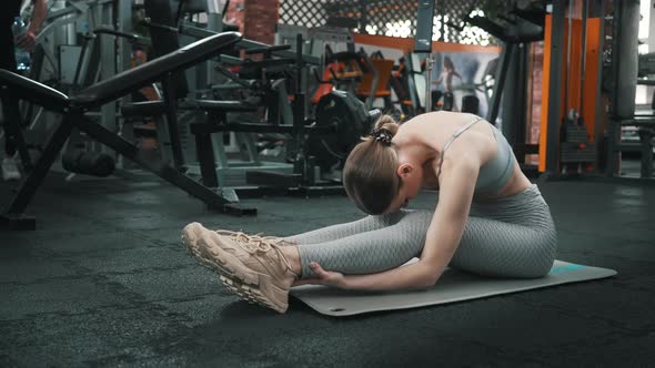 Young Thin Caucasian Woman Stretching Leg and Back Muscles After a Workout at the Local Gym While