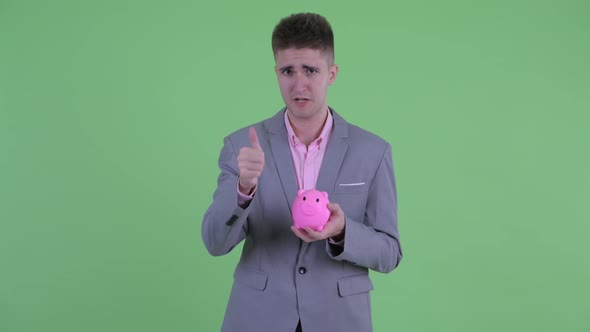 Happy Young Businessman Holding Piggy Bank and Giving Thumbs Up