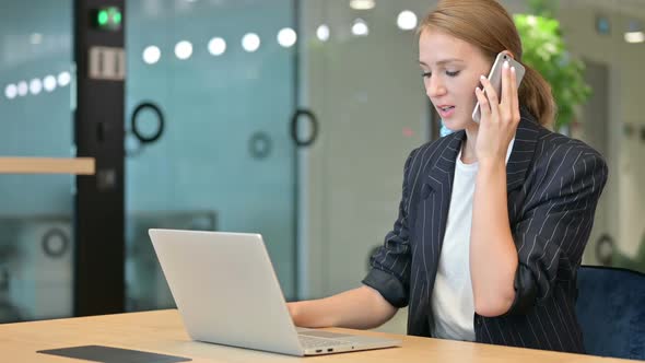 Young Businesswoman with Laptop Talking on Smartphone