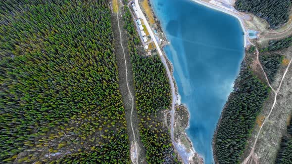 Drone footage of smooth blue lake surrounded by dense forest and trails in Alberta, Canada